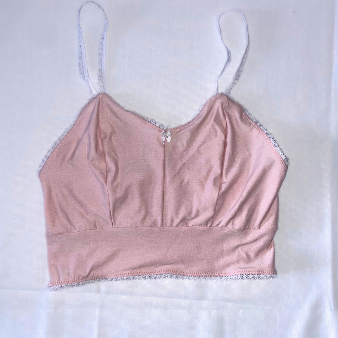 A pink camisole top with adjustable white straps and lace detailing along the neckline and hem.